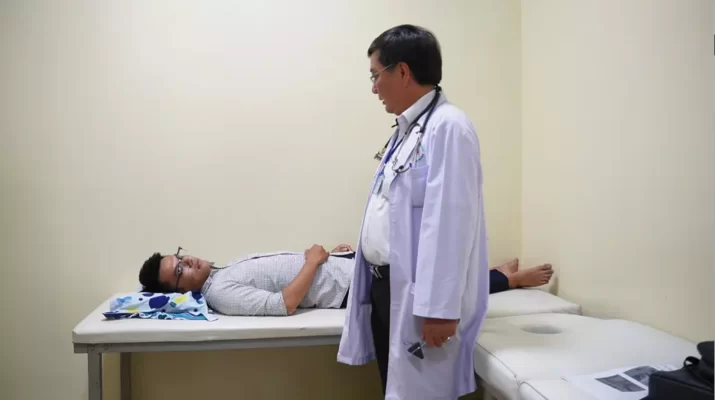 Hình ảnh bác sĩ mặc áo Blouse trắng đi chăm sóc kiểm tra bệnh nhân đang nằm tại giường bệnh điều trị cơ xương khớp 